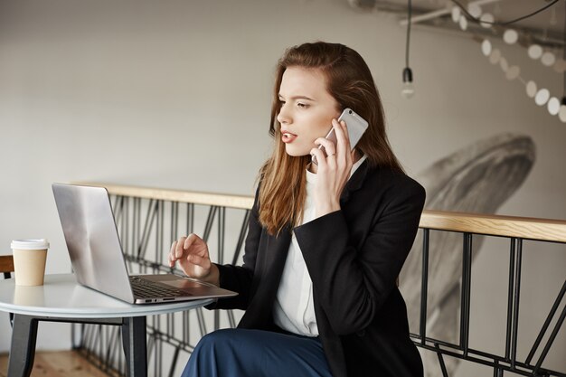 Деловая женщина, работающая в кафе, отвечает на звонки и смотрит на ноутбук