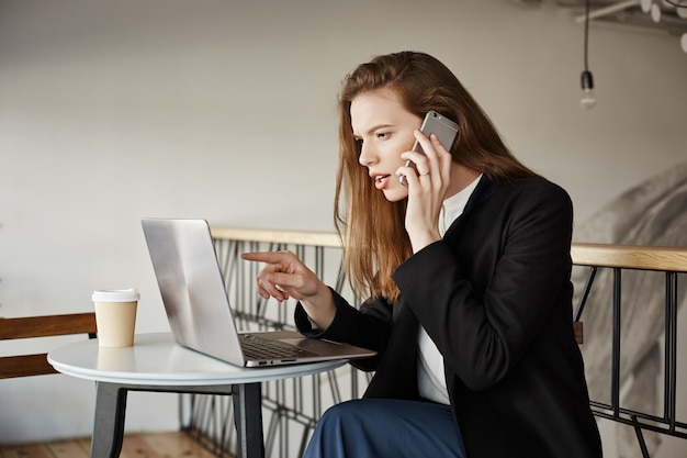 Businesswoman working in cafe, talking on phone and looking at laptop