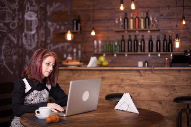 아늑한 커피숍에서 노트북 작업을 하는 사업가입니다. 그녀는 그녀의 옆에 커피 컵과 크로와상을 가지고 있습니다
