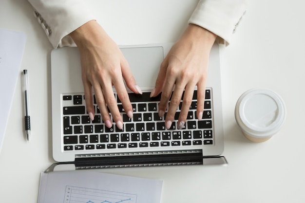 Businesswoman working on laptop, hands typing on keyboard, top view