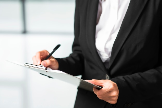 A businesswoman writing on clipboard with black pen