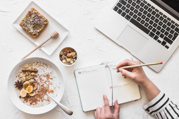 ラップトップと健康的な朝食と職場で鉛筆で日記を書くビジネスマン