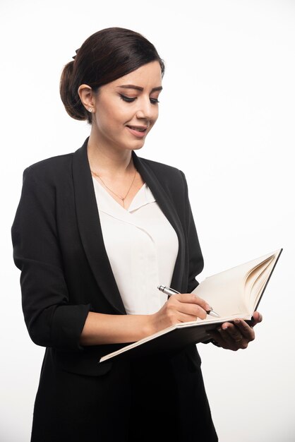 Businesswoman writing in notebook on white wall.