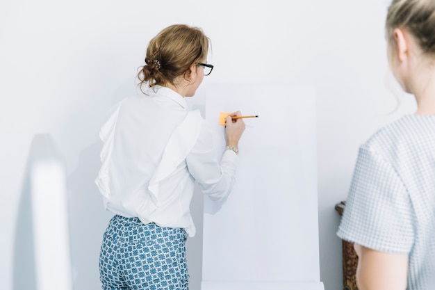 Businesswoman writing on sticky notes with pencil over white board