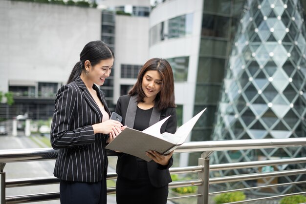 Businesswomen discussing over paperwork together against railing. Business people concept.