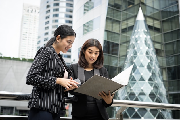 Free photo businesswomen discussing over paperwork together against railing. business people concept.