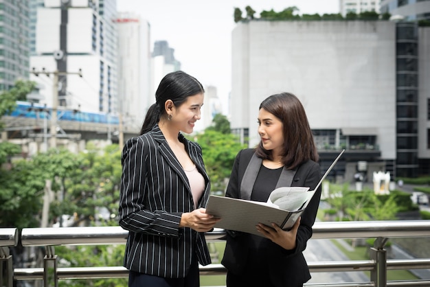 Businesswomen discussing over paperwork together against railing. Business people concept.