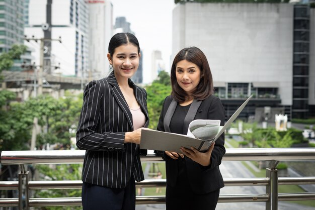 Businesswomen discussing over paperwork together against railing. Business people concept.