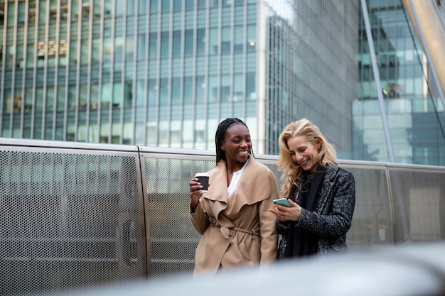 Businesswomen going to work together in the city while talking and drinking coffee