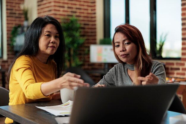 경영 프로젝트에서 일하는 여성 사업가들은 스타트업 사무실에서 회의를 하는 동안 노트북 컴퓨터에 대한 통계를 분석하고 아이디어를 브레인스토밍합니다. 함께 협력하는 경영진