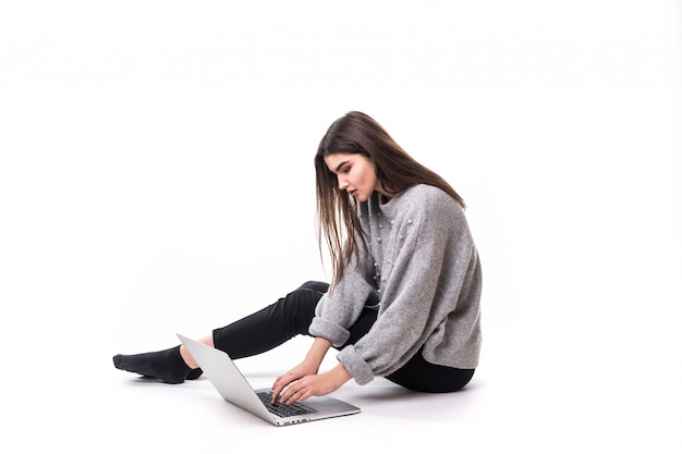 Занятая брюнетка девушка модель в сером свитере сидит на полу и работает в студии на своем ноутбуке