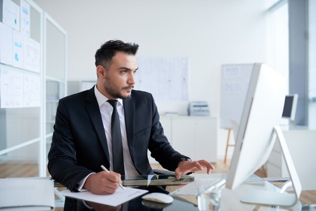 Busy Caucasian man in suit sitting in office and working on computer