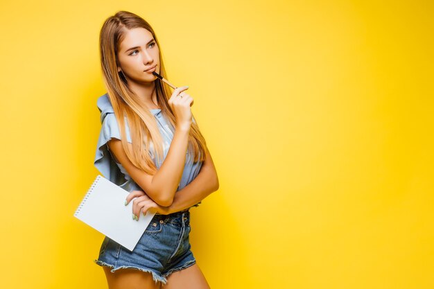 Busy charming attractive woman writing notes on notepad wearing trendy stylish blue T-shirt isolated on yellow wall