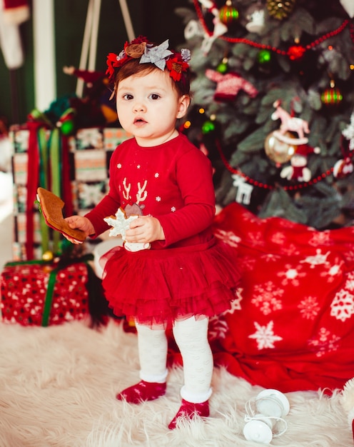 Busy child with cookies stands before Christmas tree 