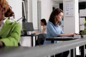 Free photo busy company employee working at desk in coworking space, corporate manager at workplace, side view. attractive serious woman typing on laptop in modern office, selective focus