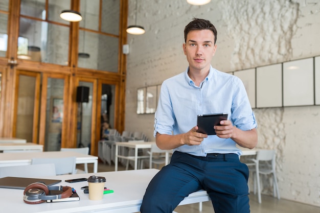 Busy confident young stylish smiling man in co-working office, startup freelancer holding using tablet,