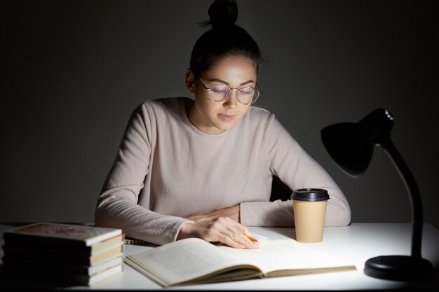 Busy female teenager reads book, uses table lamp