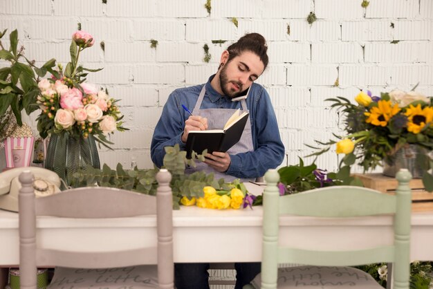 Busy male florist taking order on mobile phone and writing it down on notebook