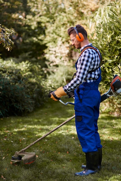 Free photo busy man using a weedwacker at garden