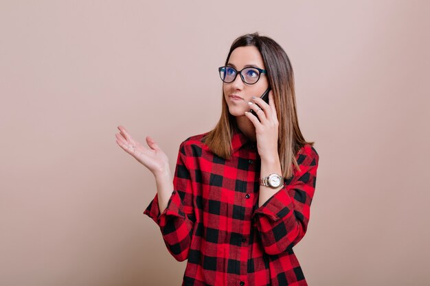 Busy modern woman wears glasses talking on smartphone with true emotions os isolated wall