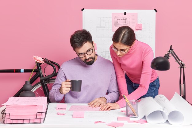 Busy woman and man office workers have brainstorming session share ideas for homework project pose in coworking space pose at desktop with blueprints around communicate together at office company