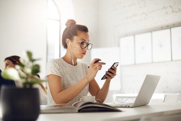 Занятая женщина с помощью смартфона и ноутбука ведет онлайн-деловой разговор в кафе или коворкинг-платформе, пьет кофе Бизнес-концепция