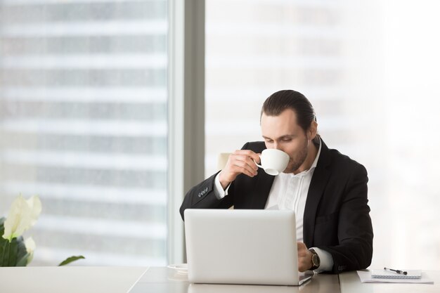Busy young businessman drinks coffee 