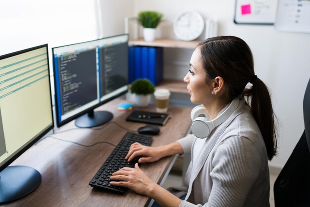 コンピューターで入力し、ソフトウェアアプリのコードを書く忙しい若い女性。彼女のオフィスの机で自宅から働くプログラマー