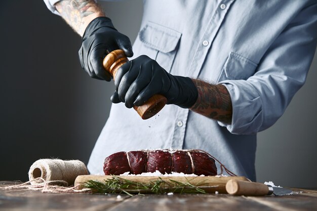 Butcher pepper tied piece of steak meat to smoke, closeup