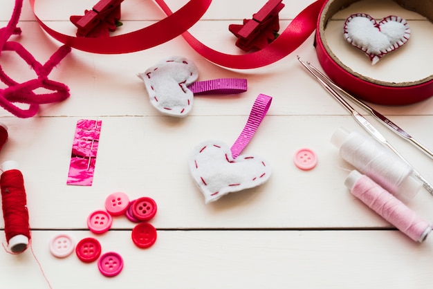 Buttons; crochet needles; thread reels; ribbons for sewing heart shape from fabric on wooden table