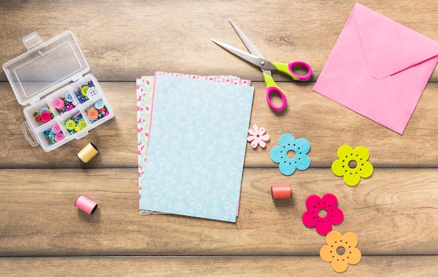 Buttons; spool and colorful paper with scissor on wooden table