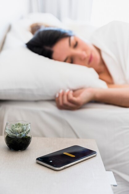 サボテンの植物とベッドで寝ている女性の近くのテーブルの上のスマートフォン