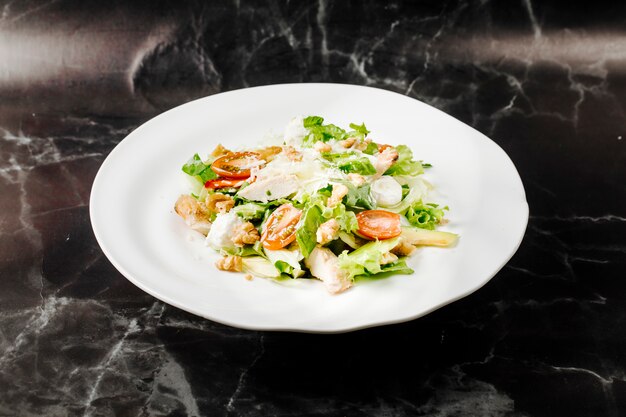 Caesar salad with mixed ingredienst inside white plate on a black marble.