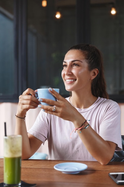 カフェの外食とランチのコンセプトレストランのテーブルに座ってコーヒーを飲みながら、世界中を旅する休暇のバックパッキング中に楽園の島バリの景色を楽しむ魅力的なヨーロッパの女性