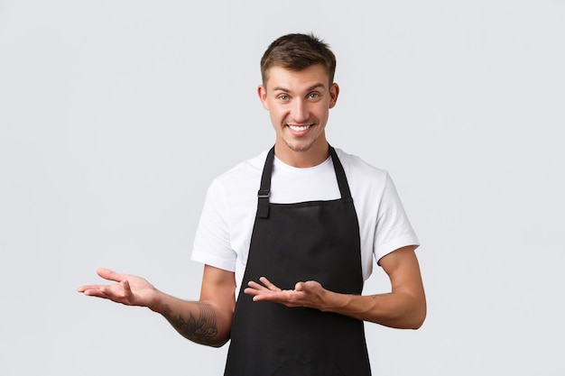 Cafe and restaurants, coffee shop owners, retail concept. Handsome cheeky salesman, waiter in black apron pointing left, inviting come inside, showing way or introducing discounts, white background
