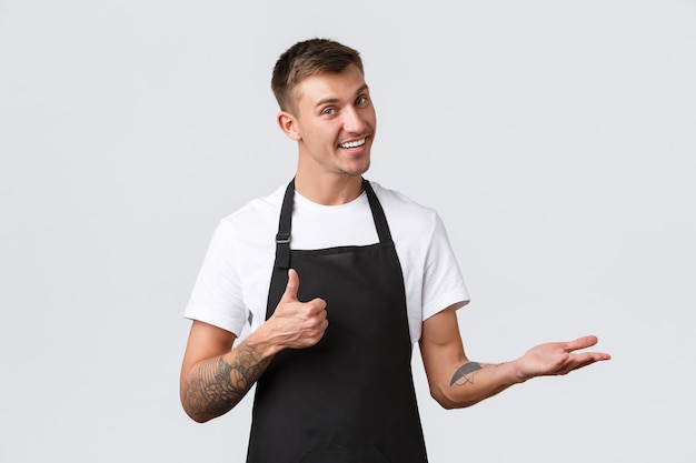 Cafe and restaurants, coffee shop owners and retail concept. Handsome smiling blond salesman, waiter or barista pointing right and showing thumbs-up, recommend, guarantee quality