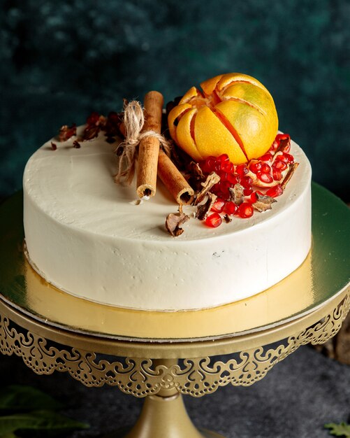 Cake covered with white cream and pomegranate, grapefruit and cinnamon sticks