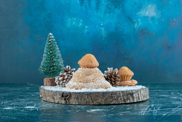 Cake, cupcakes, pine cones and a tree figurine on a board on blue.