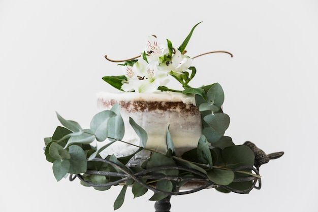 Cake decorated with alstromeria flowers and green leaves on white background