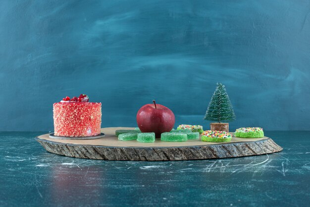 Cake, marmelades, donuts and an apple on a board on blue.