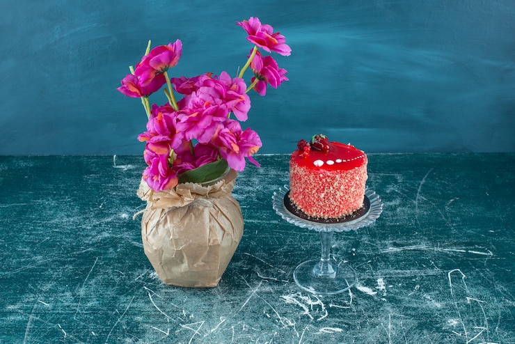 Free Photo cake on a pedestal next to a vase of flowers on blue.
