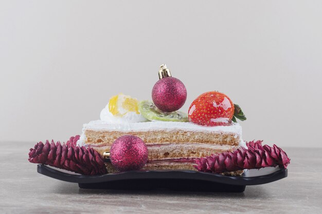 Кусочек торта на блюде, украшенном праздничными украшениями на мраморе