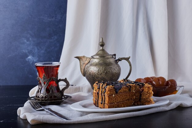 Cake slice in a white plate with chocolate syrup and tea.