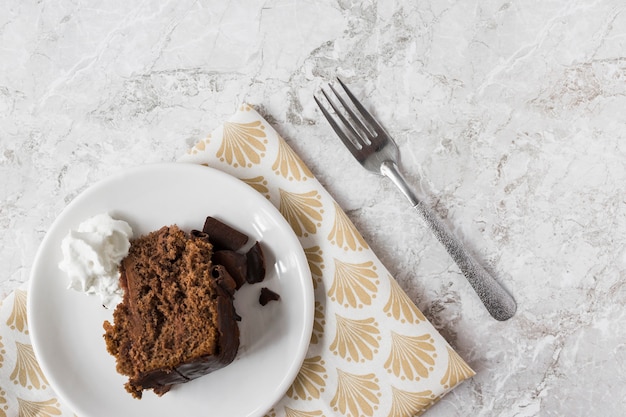 Cake slice with whipped cream on plate over the gift paper with fork