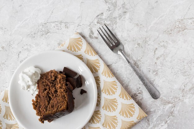 Cake slice with whipped cream on plate over the gift paper with fork