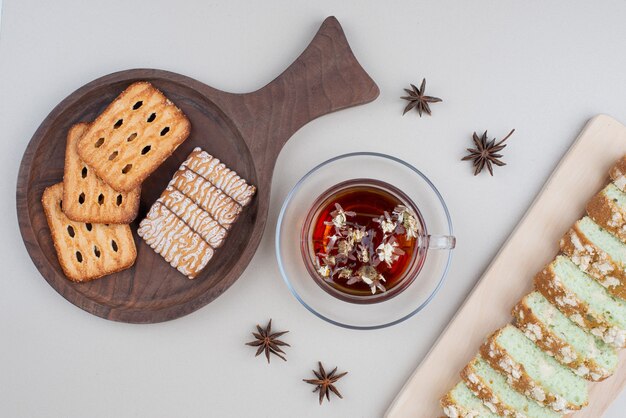 Cake slices, biscuits and cup of tea on white.