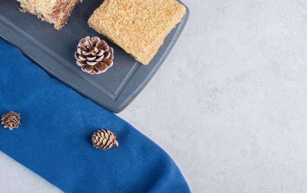 Cake slices on a navy board, with pine cones on marble surface