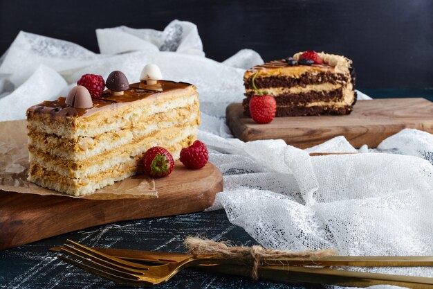 Cake slices on wooden board with berries around. 