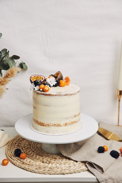 Cake with berries and passionfruits next to a plant behind a white