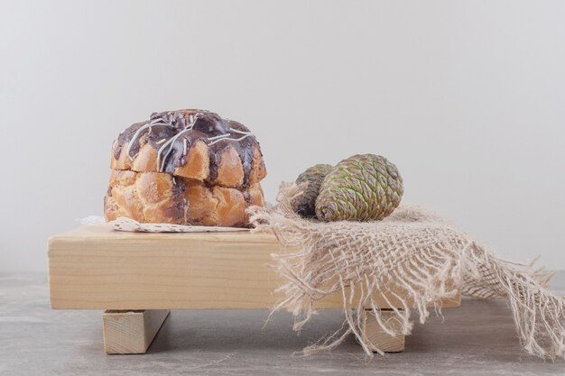 Cake with chocolate topping and two pine cones on a board on marble 